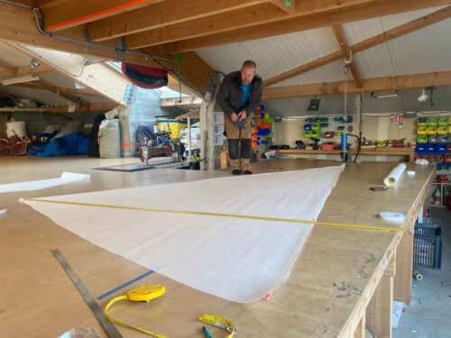 Opérateur travaillant sur une voile déployée au sol dans notre atelier de voilerie à Cherbourg